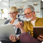 A senior couple sit in their living room and use a laptop to compare insurance policies online. 